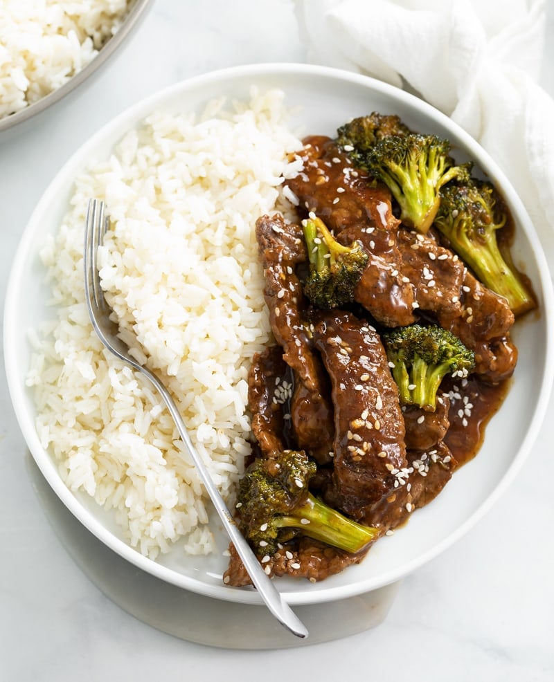 A white plate with Beef and Broccoli with rice and a fork on the side.