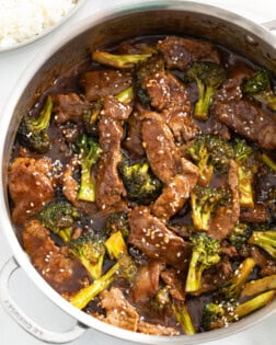 A skillet filled with beef and broccoli in a brown sauce topped with sesame seeds.