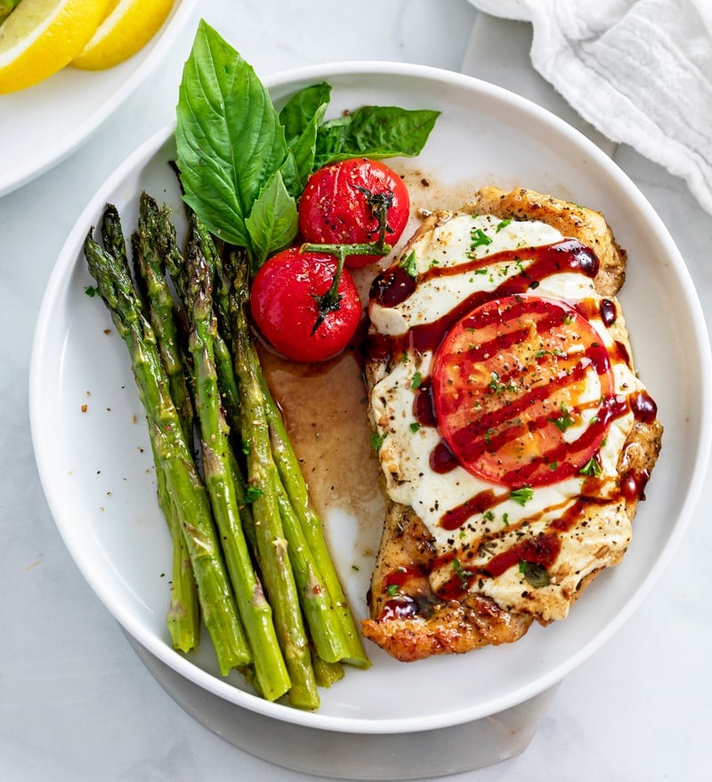 Caprese Chicken on a white plate with asparagus on the side.