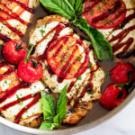 Caprese Chicken in a skillet with sauce and tomatoes and basil on top with a balsamic glaze.