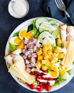 A white plate with a Chef Salad and dressing on the side.