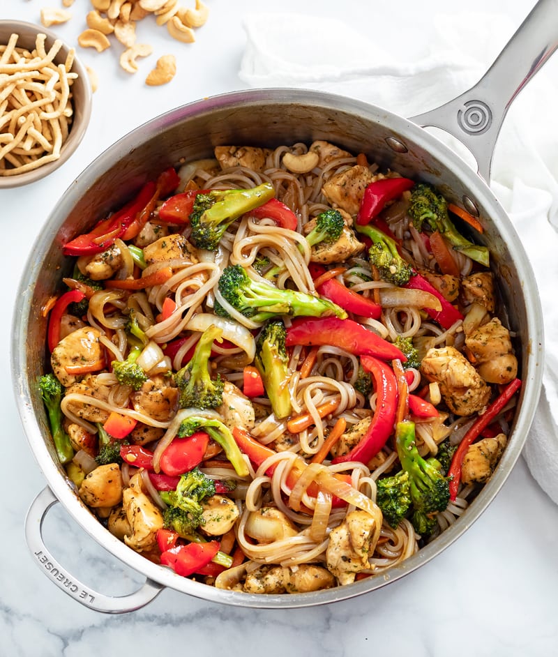 A skillet with Chicken Noodle Stir Fry with Chow Mein Noodles and Cashews on the side.