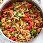 A skillet with Chicken Noodle Stir Fry with vegetables, rice noodles, and sauce.