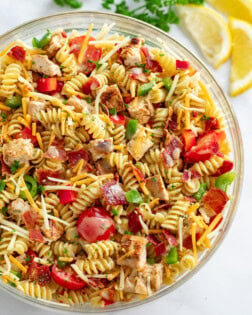 A glass bowl filled with Chicken Pasta Salad with bacon, tomatoes, cheese, and peppers.