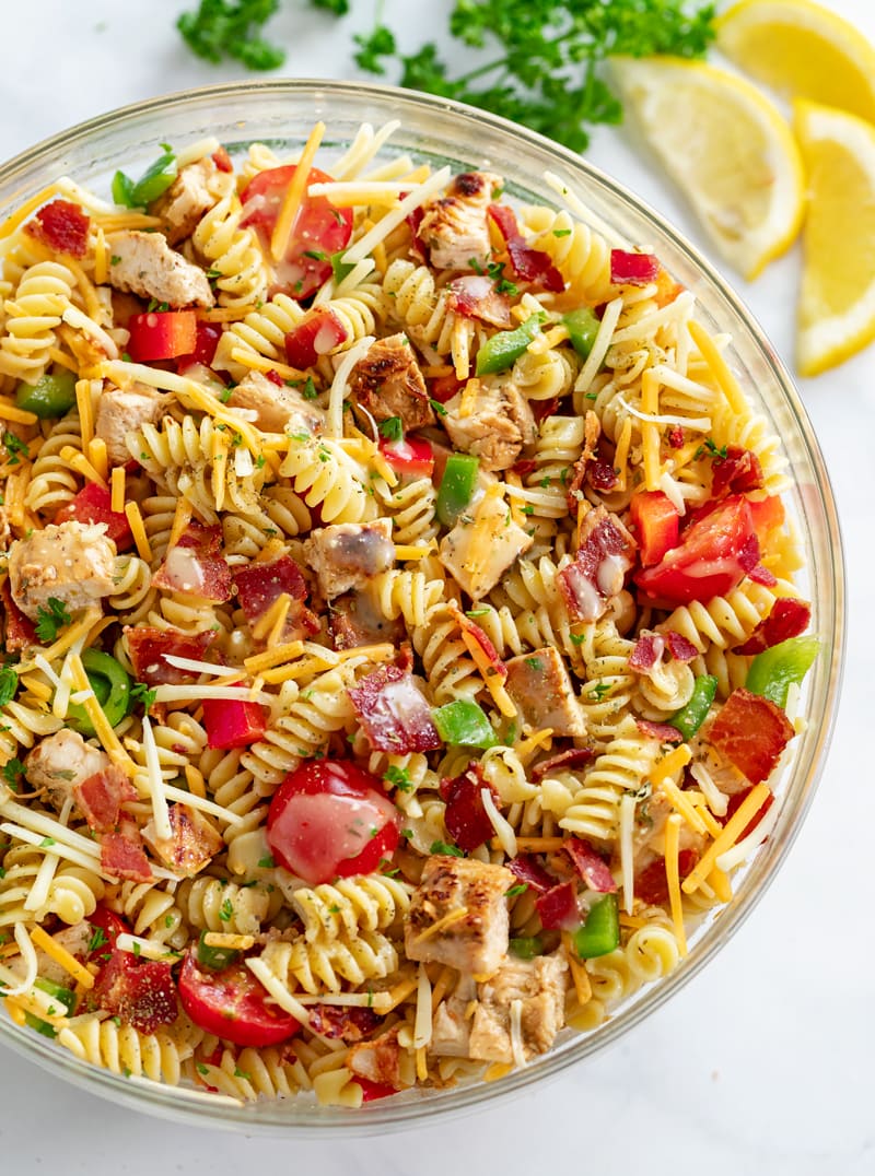 A glass bowl filled with Chicken Pasta Salad with bacon, tomatoes, cheese, and peppers.