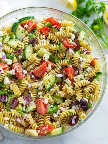 A glass bowl filled with Greek Pasta Salad.