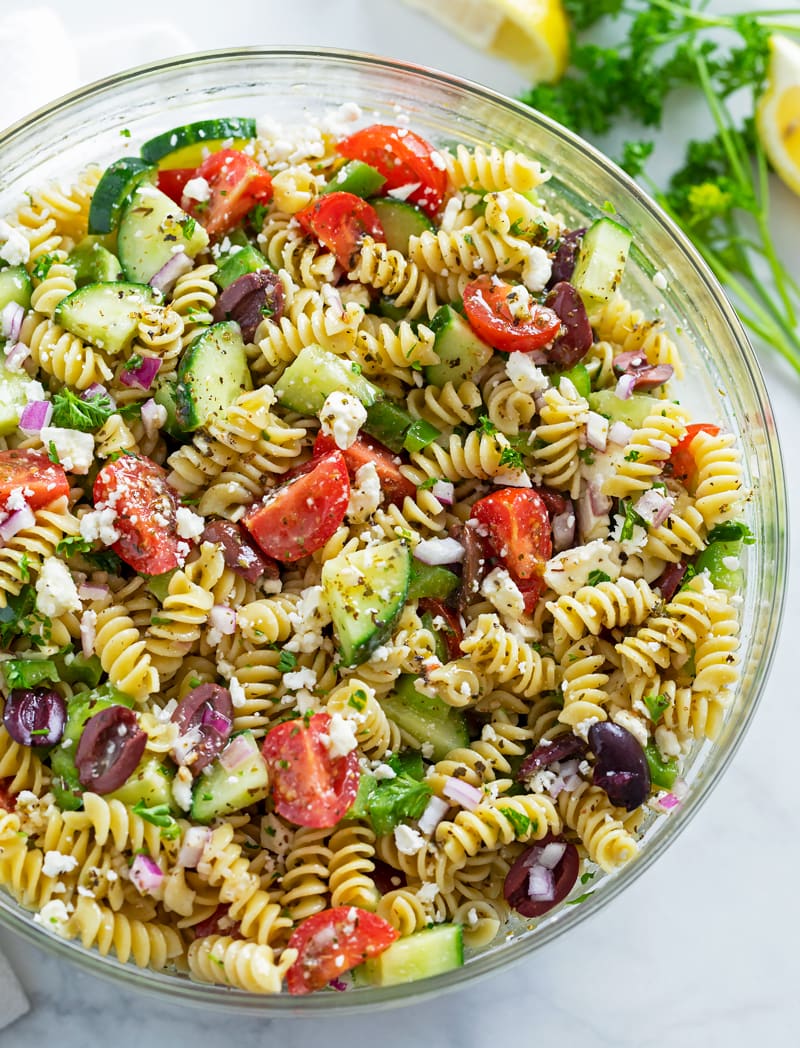 A glass bowl filled with Greek Pasta Salad.