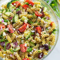 A large glass bowl filled with Greek Pasta Salad.