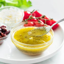 Greek salad dressing in a glass bowl with a spoon drizzling it.