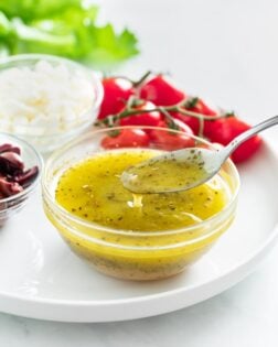 Greek salad dressing in a glass bowl with a spoon drizzling it.