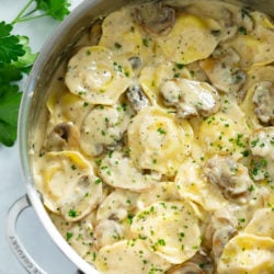 A skillet filled with ravioli in a creamy mushroom sauce with fresh parsley on top.