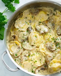 A skillet filled with ravioli in a creamy mushroom sauce with fresh parsley on top.