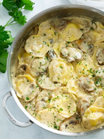 A skillet filled with ravioli in a creamy mushroom sauce with fresh parsley on top.