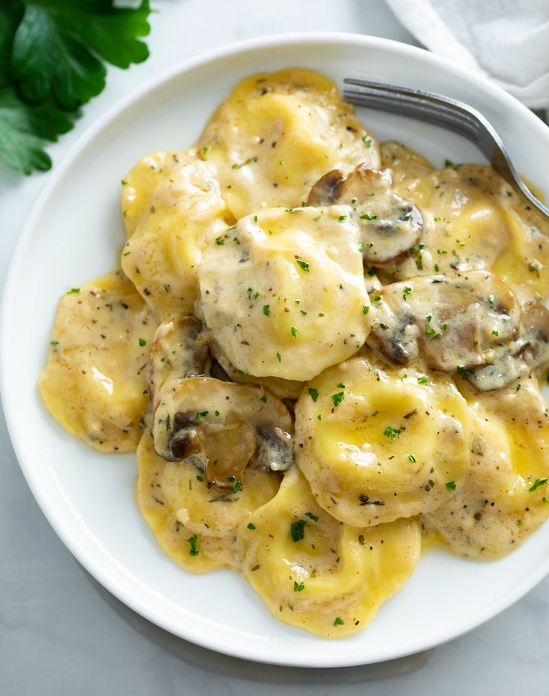 A white plate with ravioli in a creamy mushroom sauce.