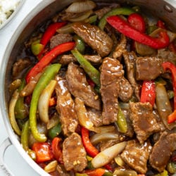 A skillet filled with Pepper Steak in a savory sauce with onions and peppers.