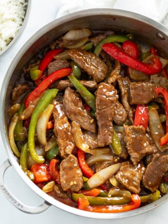 A skillet filled with Pepper Steak in a brown sauce with onions and peppers.