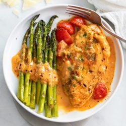 Creamy Tomato Chicken on a white plate next to asparagus with cherry tomatoes.