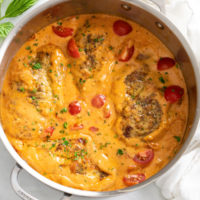 A skillet filled with Tomato Chicken in a creamy tomato sauce with cherry tomatoes.