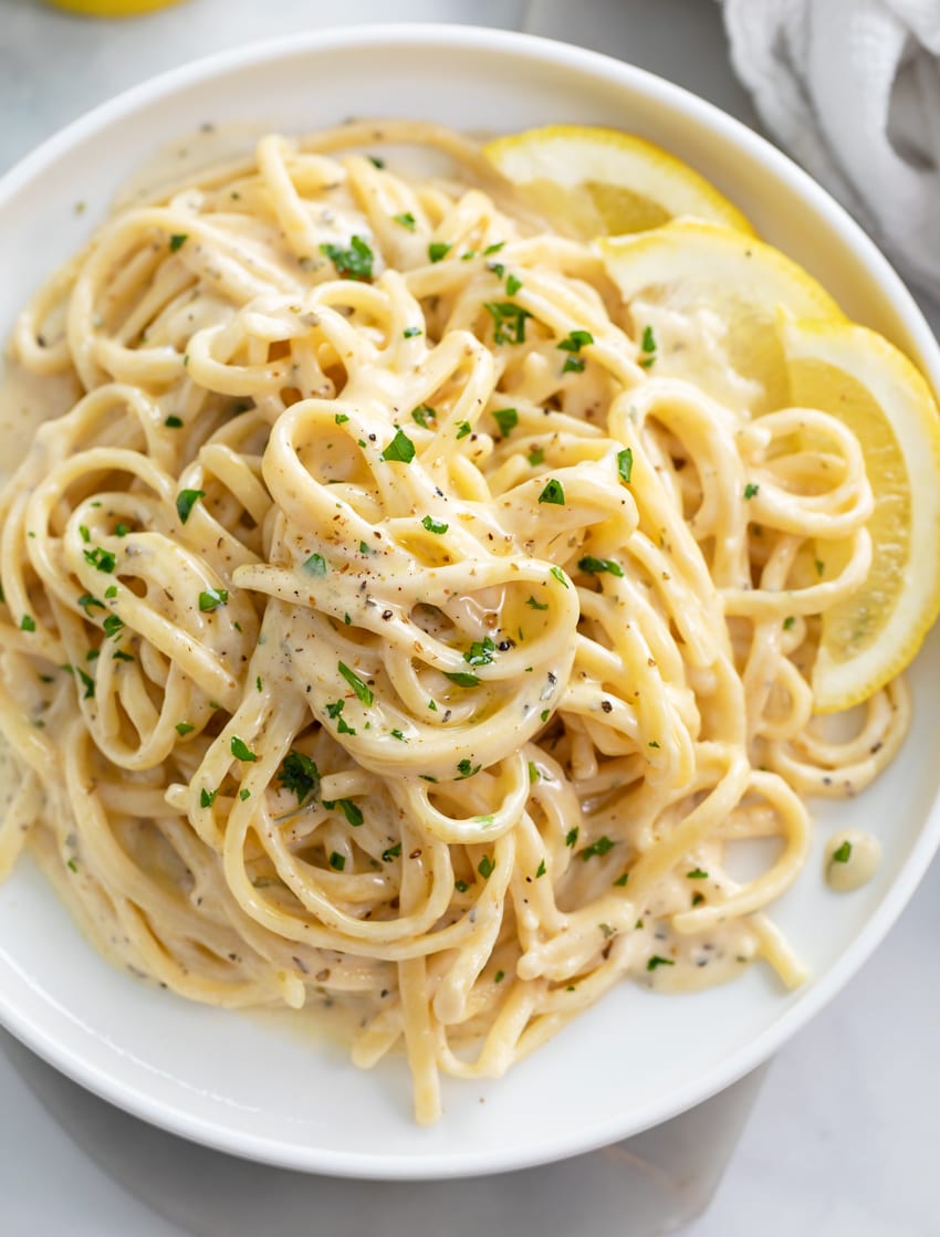 A white plate topped with Creamy Herb Pasta with lemon wedges on the side.