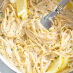 A skillet filled with Creamy Herb Pasta with lemon slices and kitchen tongs.