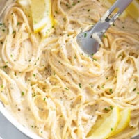 A skillet filled with Creamy Herb Pasta with lemon slices and kitchen tongs.