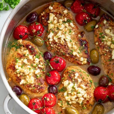 A skillet filled with Greek Chicken in sauce with Feta, tomatoes, and olives.