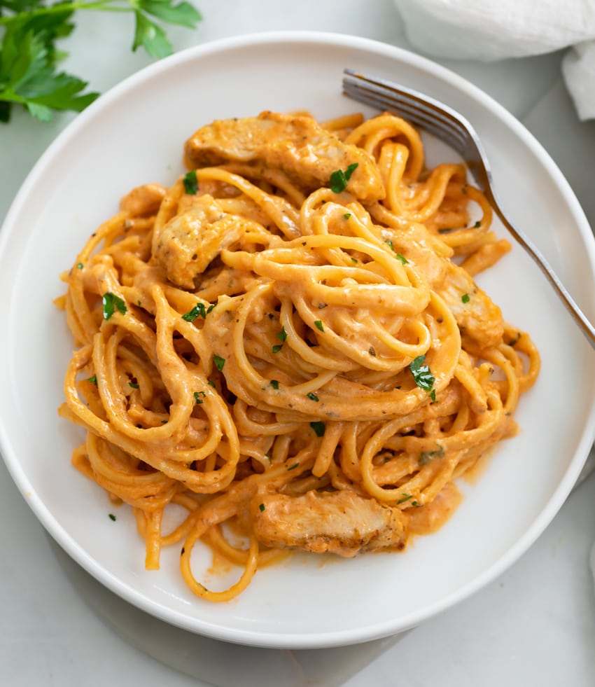 A white plate with Creamy Tomato Pasta and chicken with a fork on the side.
