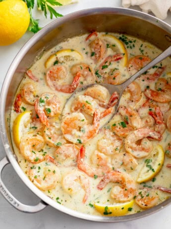 Creamy Garlic Shrimp in a skillet with lemons and chopped parsley.