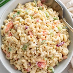 A white bowl filled with creamy Macaroni Salad with a spoon on the side.