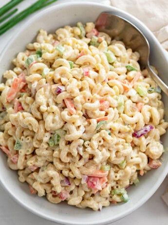 A white bowl filled with creamy Macaroni Salad with a spoon on the side.