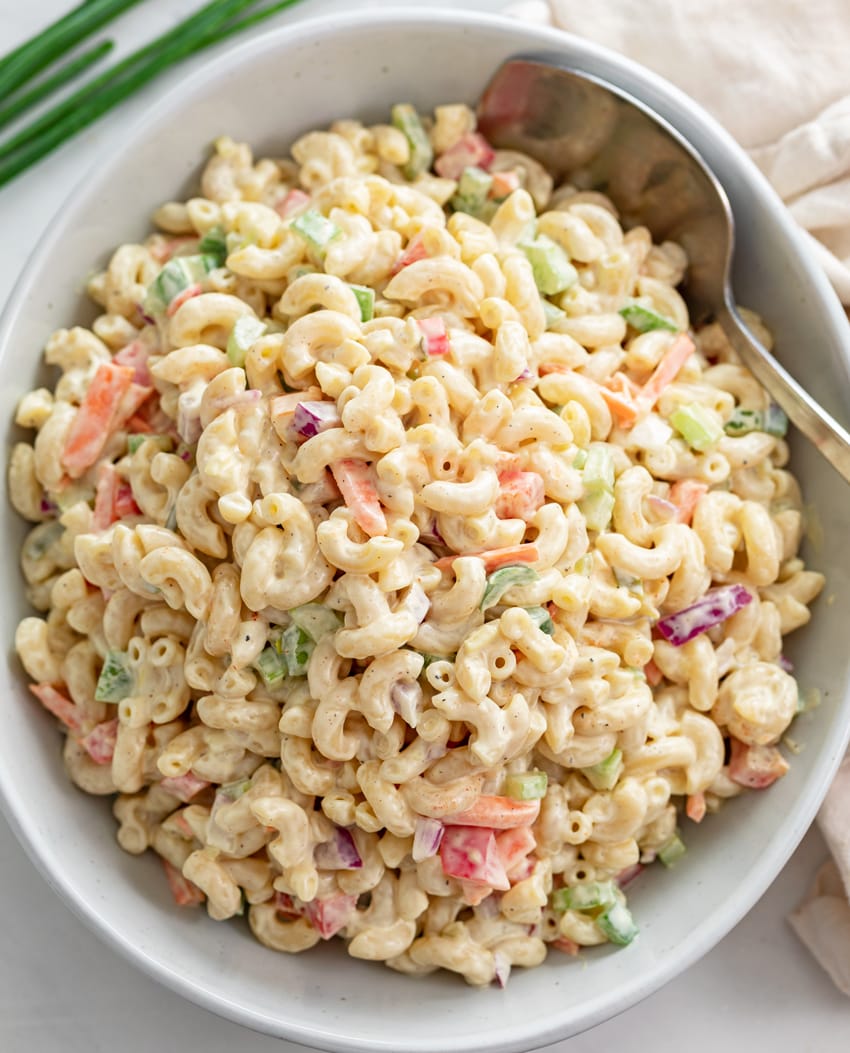 A white bowl filled with creamy Macaroni Salad with a spoon on the side.
