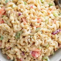 Creamy Macaroni Salad in a white bowl with slices of carrots, celery, and onions.