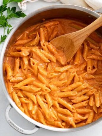 A skillet filled with Pink Sauce Pasta with a wooden spoon.