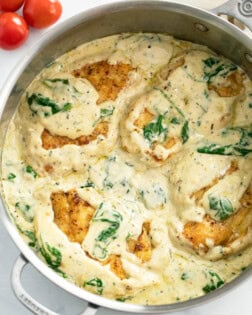 A skillet filled with creamy Spinach Chicken with cherry tomatoes on the side.