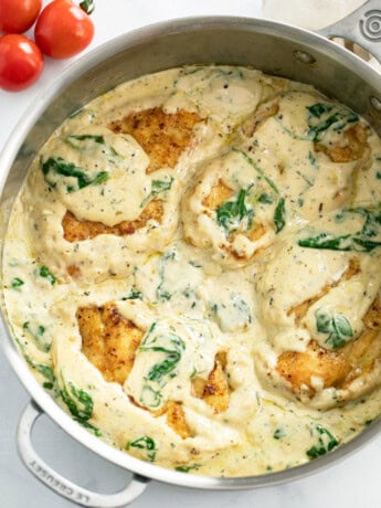 A skillet filled with creamy Spinach Chicken with cherry tomatoes on the side.