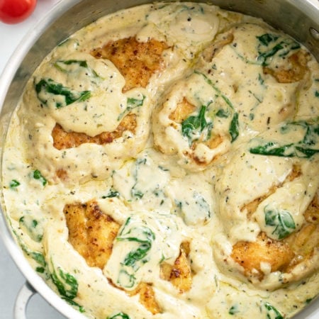 A skillet filled with creamy Spinach Chicken with cherry tomatoes on the side.