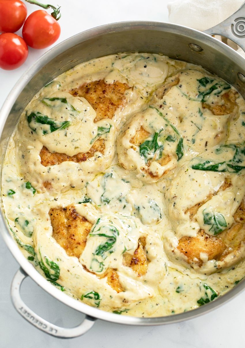 A skillet filled with creamy Spinach Chicken with cherry tomatoes on the side.