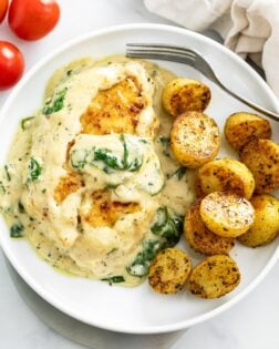 Creamy Spinach Chicken on a white plate with roasted potatoes and a fork.