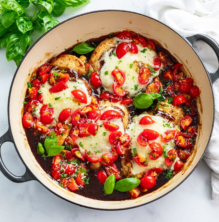 Bruschetta Chicken in a skillet with Balsamic sauce, diced tomatoes, and basil.