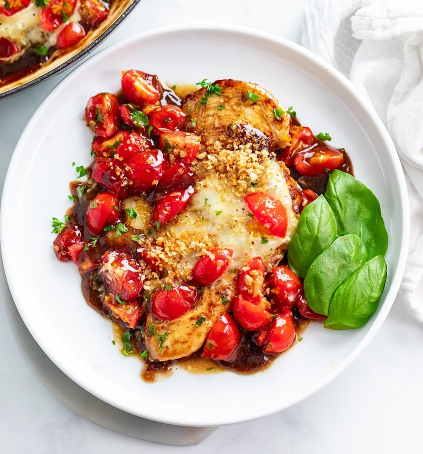 A plate of Bruschetta Chicken with melted cheese, diced tomatoes, and basil.