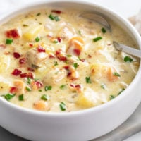 Chicken Potato Soup in a white bowl with a spoon on the side and bacon and chives on top.
