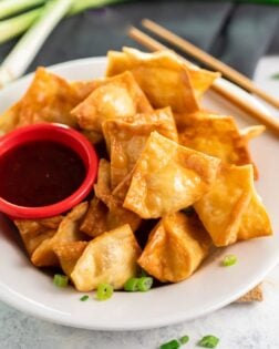 Crab Rangoon on a white plate with dipping sauce.