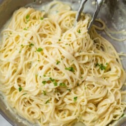 A skillet with Garlic Parmesan Pasta with kitchen tongs.