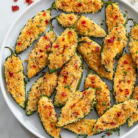 Jalapeno Poppers on a white plate topped with crispy panko breadcrumbs and bacon.