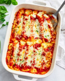 Cheese filled manicotti in a white casserole dish with a spatula on the side.