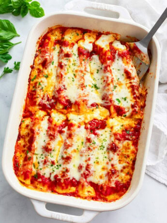 Cheese filled manicotti in a white casserole dish with a spatula on the side.