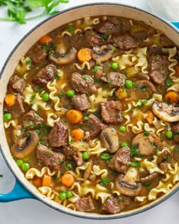 A soup pot filled with Beef Noodle Soup with mushrooms, carrots, noodles, and beef.