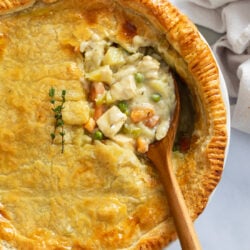 Chicken Pot Pie in a pie pan with the filling being scooped up with a wooden spoon.