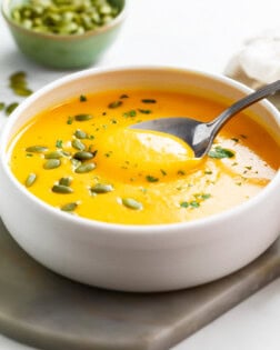 Roasted Butternut Squash Soup in a white bowl with a spoon and pumpkin seeds on top.