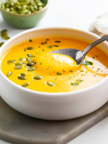 Roasted Butternut Squash Soup in a white bowl with a spoon and pumpkin seeds on top.